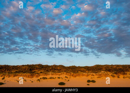 A cluster of clouds gather over a sand dune at sunset. Stock Photo