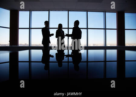 Outlines of three office workers interacting by the window Stock Photo