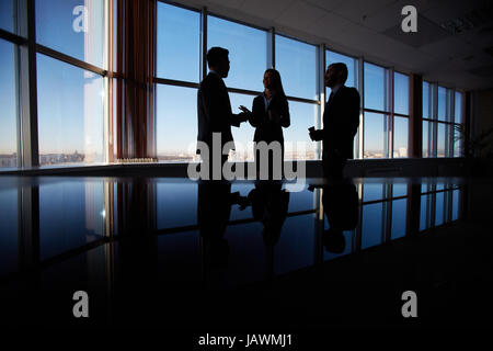 Outlines of three office workers interacting by the window Stock Photo