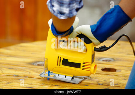Close up of a man wearing job gloves working wood with electric jigsaw Stock Photo