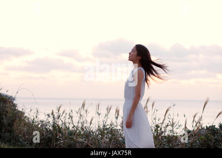 Young Japanese woman in a white dress at a cliff over the sea at sunrise, Chiba, Japan Stock Photo