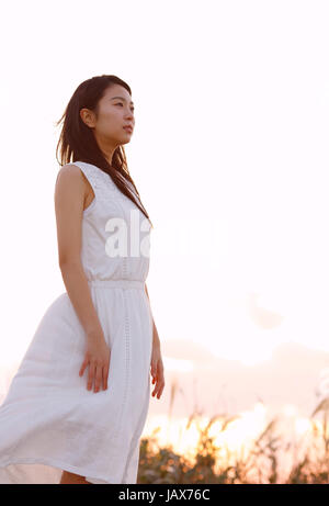 Young Japanese woman in a white dress at a cliff over the sea at sunrise, Chiba, Japan Stock Photo