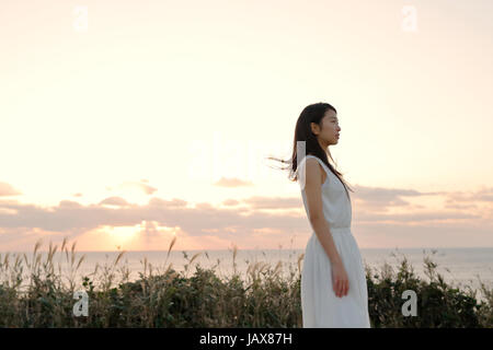 Young Japanese woman in a white dress at a cliff over the sea at sunrise, Chiba, Japan Stock Photo