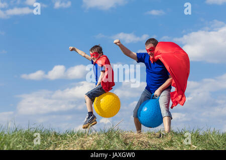 Father and son playing superhero at the day time. People having fun outdoors.They jumping on inflatable balls on the lawn. Concept of friendly family. Stock Photo