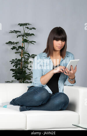 Junge, hübsche Frau sitzt auf dem Sofa und liest ein Ebook Stock Photo