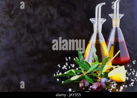 Grey abstract background with olive oil and wine vinegar glass jars with lemon, sea salt, garlic and olive branch. Space for text. Stock Photo