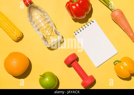 Fitness concept. Collection of fresh fruits with dumbells and water bottle on yellow background. Stock Photo