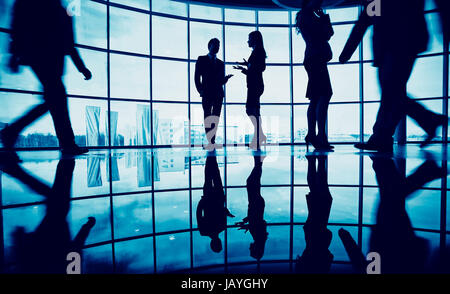 Several white collar workers communicating in office against window with two businessmen walking around Stock Photo