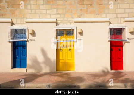 Three brightly coloured blue yellow and red front doors on an appartment building in the fishing port of Marsaxlokk Malta Stock Photo