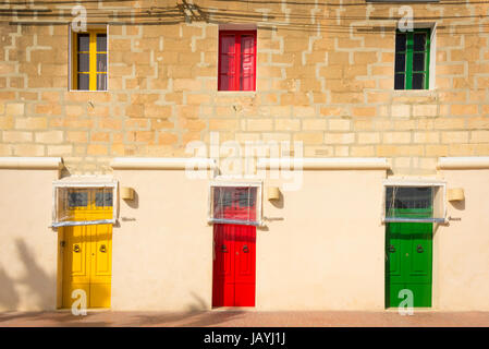 Three brightly coloured blue yellow and red front doors on an appartment building in the fishing port of Marsaxlokk Malta Stock Photo