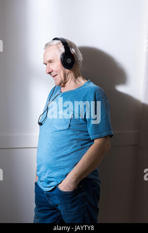 Pensive senior man with hands in pockets wearing headphones Stock Photo