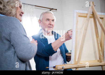 Happy senior couple painting picture on easel at home Stock Photo