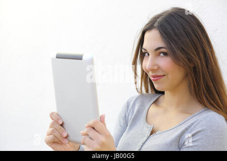 Pretty woman holding a tablet and looking at camera on a white wall Stock Photo
