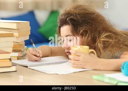Tired and sleepy student with tousled hair trying to write notes on a desk in her room in a house indoor Stock Photo