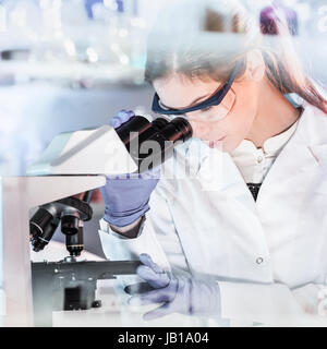 Life scientists researching in laboratory. Attractive female young scientist microscoping in their working environment. Healthcare and biotechnology. Stock Photo