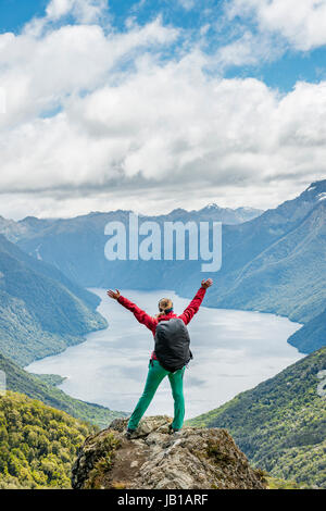 Female hiker is looking at the South Fiord of Lake Te Anau, stretching arms in the air, at back the Southern Alps