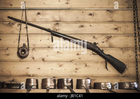 Old hunting rifle with powder flask hanging on wooden wall Stock Photo