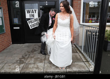 Alliance candidate for West Belfast Sorcha Eastwood casts her vote in the 2017 General Election, with her husband, Dale Shirlow, at a polling station in Lisburn, Northern Ireland, still wearing her wedding dress after they were married earlier in the day. Stock Photo