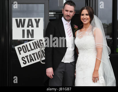 Alliance candidate for West Belfast Sorcha Eastwood casts her vote in the 2017 General Election, with her husband, Dale Shirlow, at a polling station in Lisburn, Northern Ireland, still wearing her wedding dress after they were married earlier in the day. Stock Photo