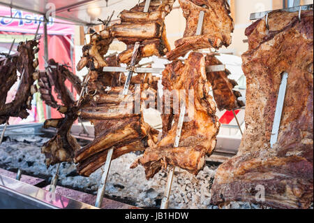 Roasted meat of beef cooked on a vertical grills placed around fire. Asado, traditional barbecue dish in Argentina Stock Photo