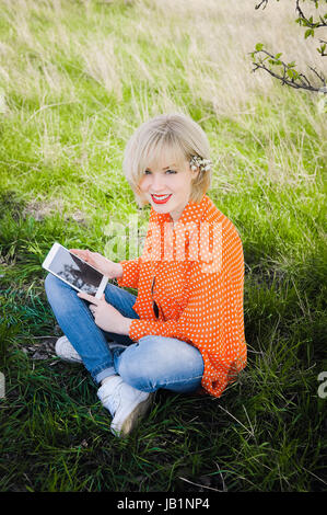 close-up portrait outdoors young beautiful girl in an orange hipster blonde bright cheerful  dot blouse , smiling red plump lips on the backgroun Stock Photo