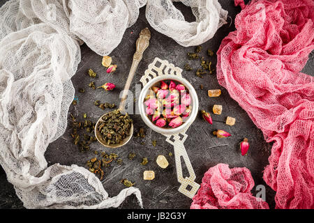 Dry rose buds in a small metal strainer, and dry green tea in the spoon and caramelized brown sugar. Stock Photo