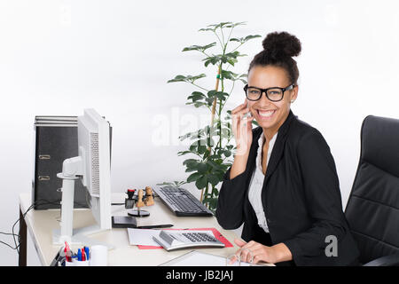 Junge, hübsche Angestellte sitzt am Schreibtisch im Büro und telefoniert mit einem Smartphone Stock Photo