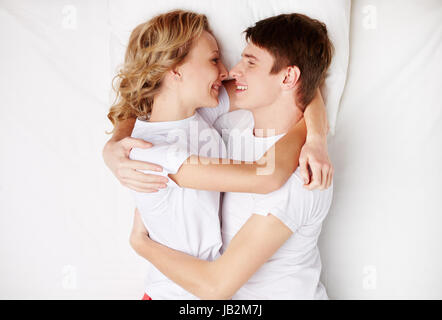 Two happy young dates lying in bed and embracing Stock Photo