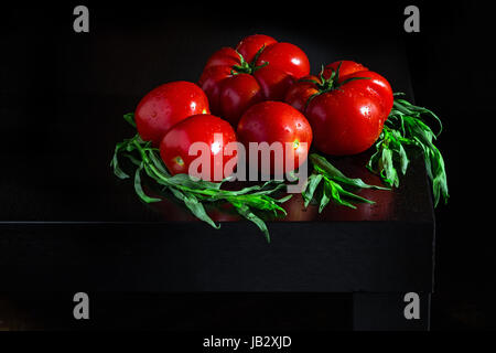 Three large fresh tomatoes . sprigs of estragon and water droplets on a dark wooden background Stock Photo