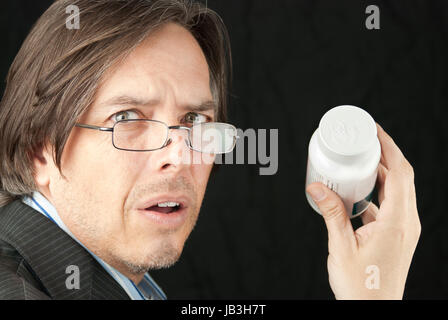 Close-up of a casual businessman wearing glasses frustrated trying to read a pill bottle label. Stock Photo