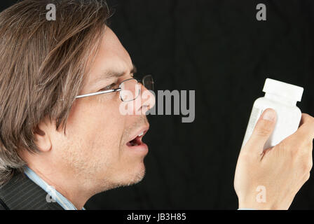 Close-up of a casual businessman wearing glasses trying to read a pill bottle label. Stock Photo