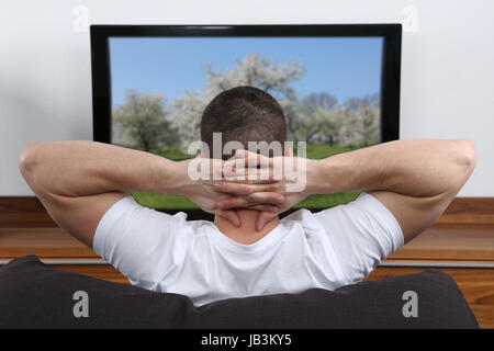 Junger Mann sitzt auf dem Sofa und schaut fernsehen Stock Photo