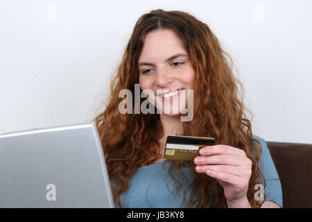 Eine junge Frau sitzt am Laptop und kauft im Internet mit einer Kreditkarte ein Stock Photo