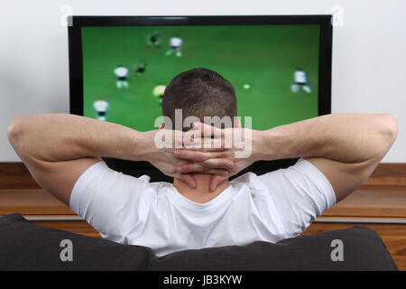 Ein junger Mann sitzt auf dem Sofa und schaut Fußball im Fernsehen Stock Photo