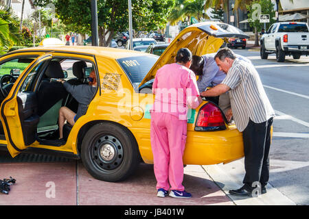 Miami Beach Florida,driveway,yellow cab,taxi,trunk,unloading,adult adults man men male,woman women female lady,passenger passengers rider riders,drive Stock Photo