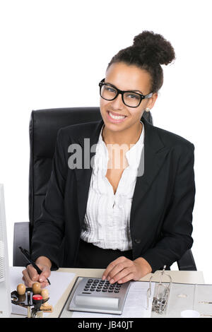 Junge, hübsche Büroangestellte sitzt am Schreibtisch im Büro und führt Berechnungen mit einem Tischrechner durch Stock Photo