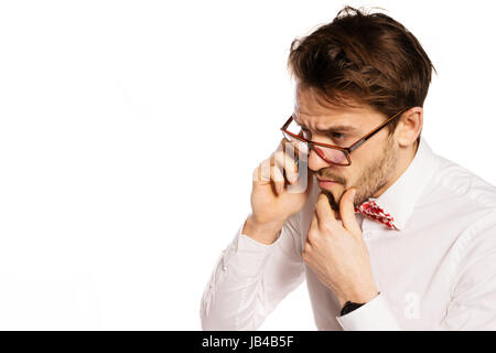 Nerdy bearded businessman wearing glasses and a polka dot bow tie frowning as he listens to the conversation while talking on a smartphone, isolated on white Stock Photo