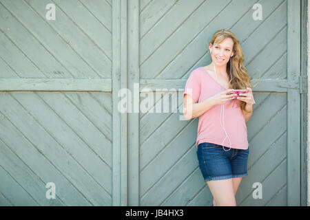 Outdoor Portrait of Young Adult Brown Eyed Woman Listening To Music with Earphones on Her Smart Phone. Stock Photo