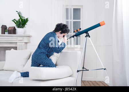 side view of focused little boy looking through telescope Stock Photo