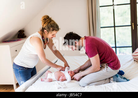 Young parents at home dressing their baby girl on bed Stock Photo