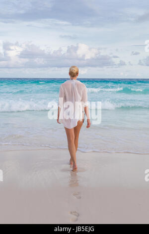 Woman wearing white loose tunic over bikini on Mahe Island, Seychelles. Summer vacations on picture perfect tropical beach concept. Stock Photo