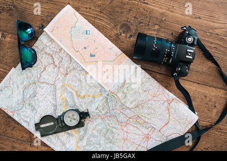 Roadtrip, exploration accessories and equipment laying on a map on a wooden table. Sunglasses, compass, camera and map Stock Photo