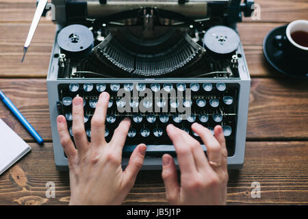 From above crop shot of person using typewriter on wooden table. Stock Photo