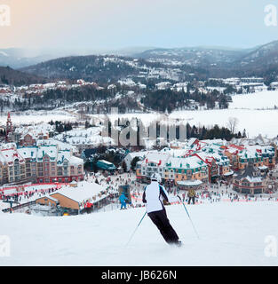 Mont-Tremblant, Canada - February 9, 2014: Skiers and snowboarders are sliding down the main slope at Mont-Tremblant. Mont-Tremblant Ski Resort is acknowledged by most industry experts as being the best ski resort in Eastern North America. Stock Photo