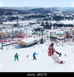 Mont-Tremblant, Canada - February 9, 2014: Skiers and snowboarders are sliding down the main slope at Mont-Tremblant. Mont-Tremblant Ski Resort is acknowledged by most industry experts as being the best ski resort in Eastern North America. Stock Photo