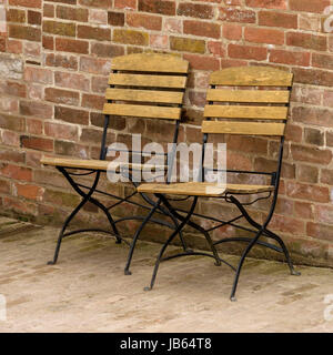 Two folding metal chairs with wooden slats in front of red brick wall. Stock Photo