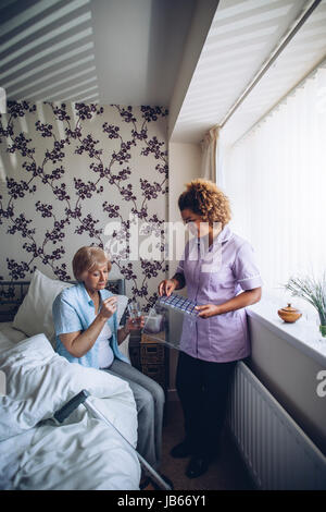 Senior woman taking her medication, with assistance from a home careworker. Stock Photo