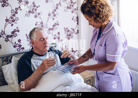 Bedbound senior man receiving assistance from a home caregiver. He is taking some medication with water. Stock Photo