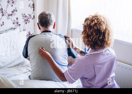 Home care nurse checking a senior mans lungs with a stethoscope against his back. Stock Photo