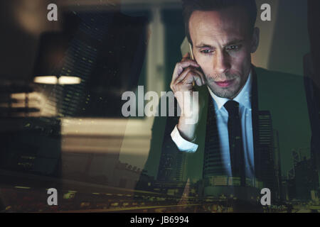 The tired businessman in the office sitting and communicating with smartphone. Stock Photo